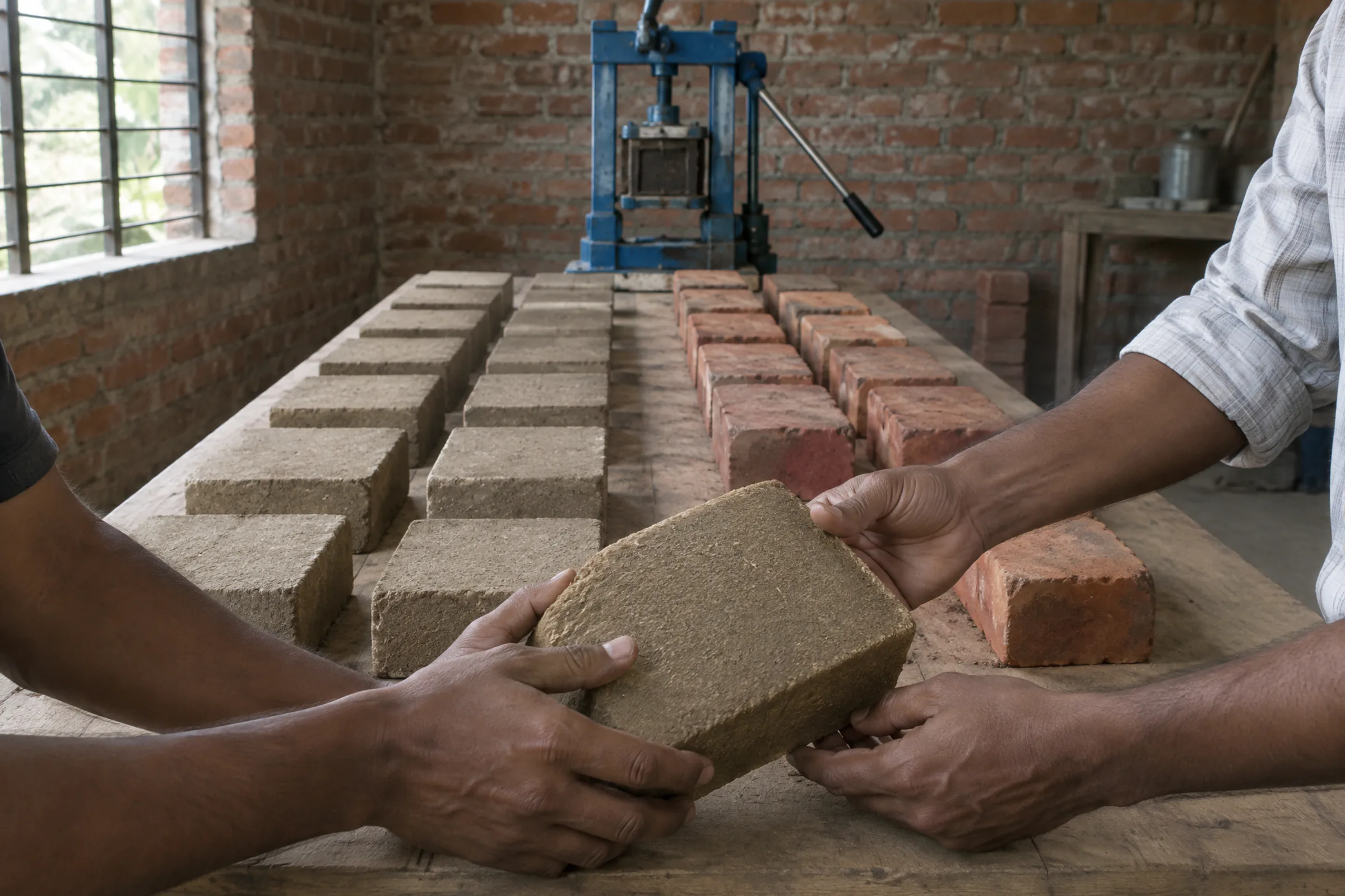 Earth blocks and bricks laid out for testing, with two people turning one block over