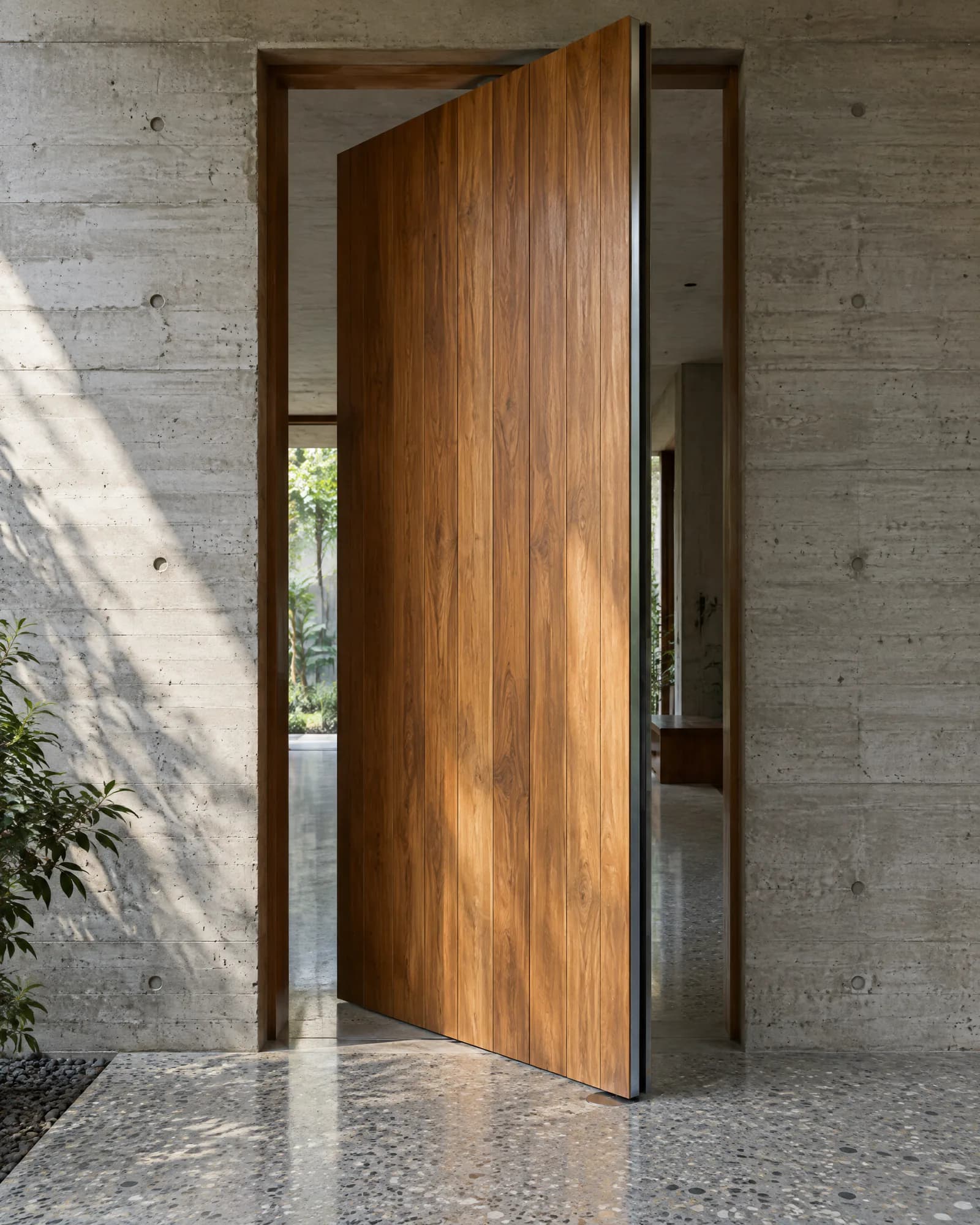 Tall teak pivot door standing partly open in a board-marked concrete wall