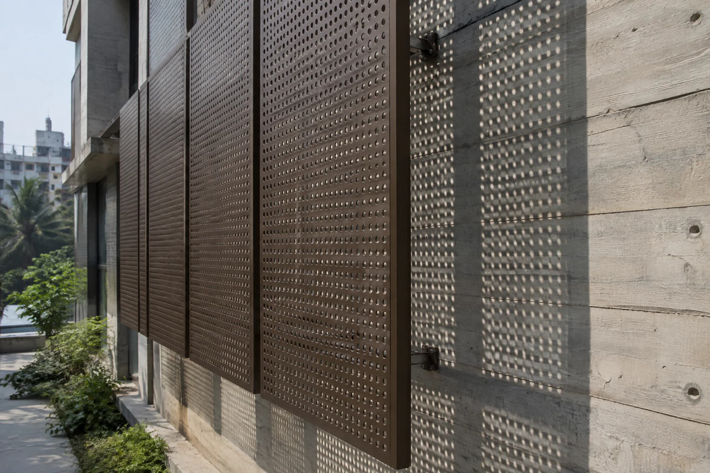 Bronze perforated metal screen casting a pattern of dots on a concrete wall