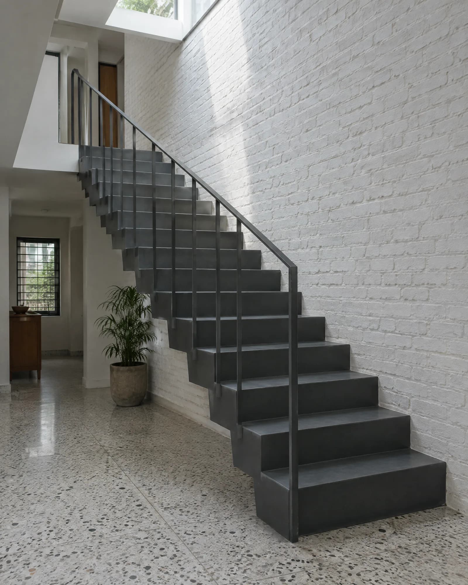 Charcoal folded steel stair rising along a white brick wall