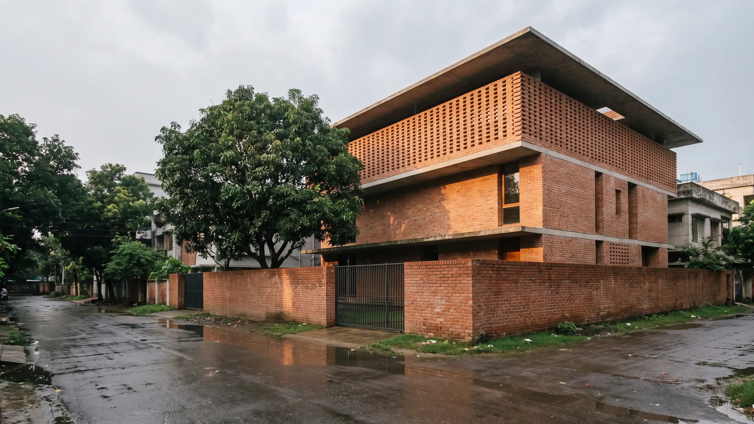 Three-storey brick house with a perforated brick screen on the upper floor, behind a mango tree after rain